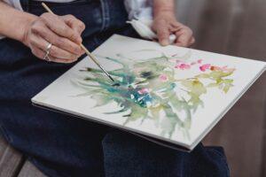 Anciana pintando flores sobre tela con pintura a base de agua.